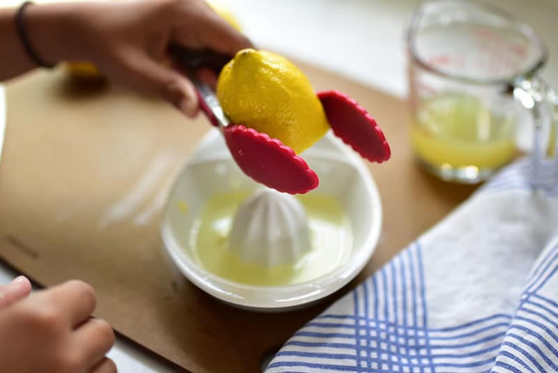 Lemon being squeezed with a set of red tongs over a lemon reamer.