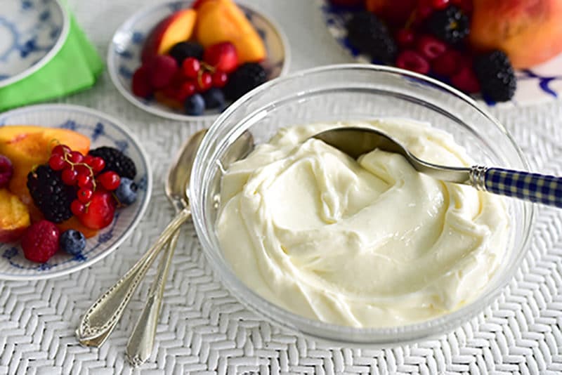 A bowl of ashta cream with a spoon, with places of fresh fruit next to it.