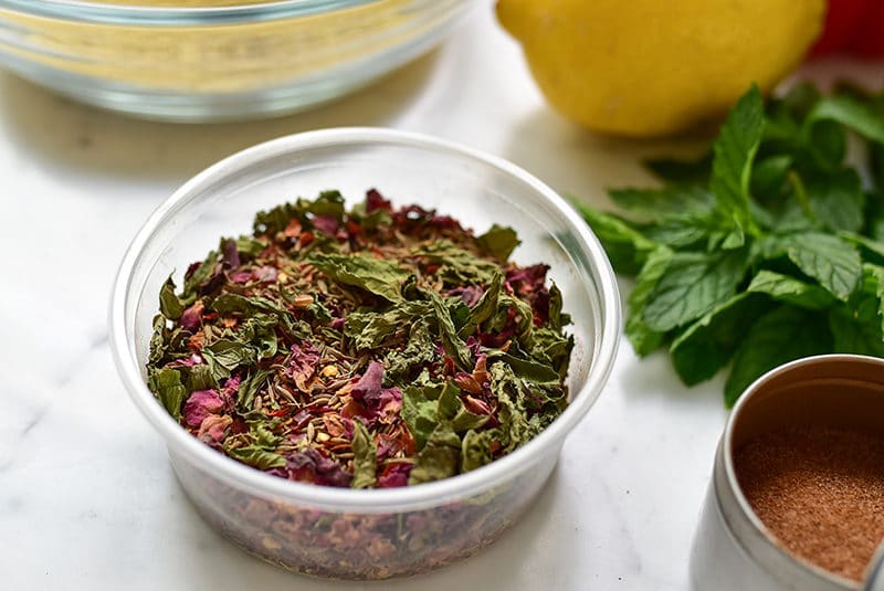 Dried mint and rose petals in kibbeh spice in a plastic container, surrounded by fresh mint and lemon, Muareen Abood