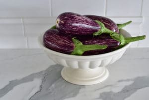 Purple eggplant in a footed dish on a marble countertop, Maureen Abood