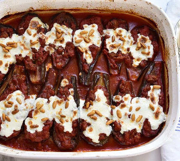 Lebanese eggplant boats in tomato sauce topped with cheese and pine nuts, in a white casserole