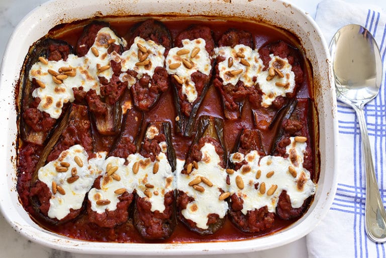 Lebanese eggplant boats in tomato sauce topped with cheese and pine nuts, in a white casserole