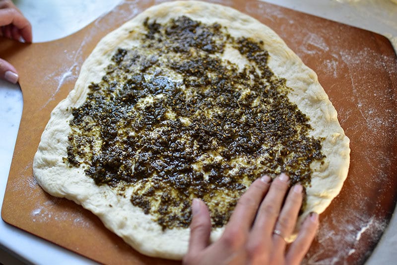 Spreading zaatar and oil on dough for zaatar flatbread