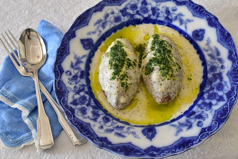 Kibbeh balls with yogurt sauce topped with olive oil and herbs in a blue dish