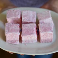 Pink square marshmallows on a white plate with hands holding it