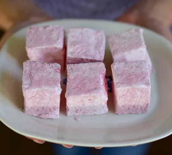 Pink square marshmallows on a white plate with hands holding it