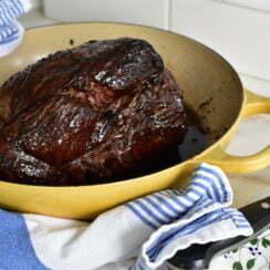 Pomegranate glazed leg of lamb in a yellow roasting dish with blue and white towel around it