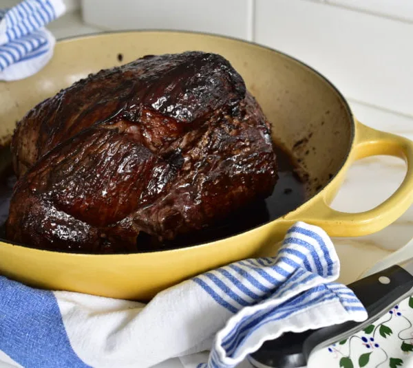 Pomegranate glazed leg of lamb in a yellow roasting dish with blue and white towel around it