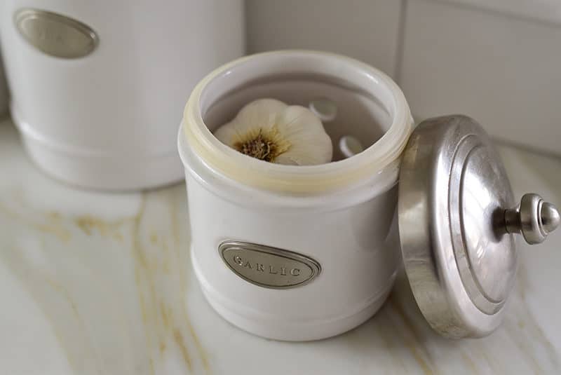 A head of garlic in a small white containter with a metal lid