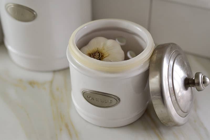 A head of garlic in a small white container with a metal lid.