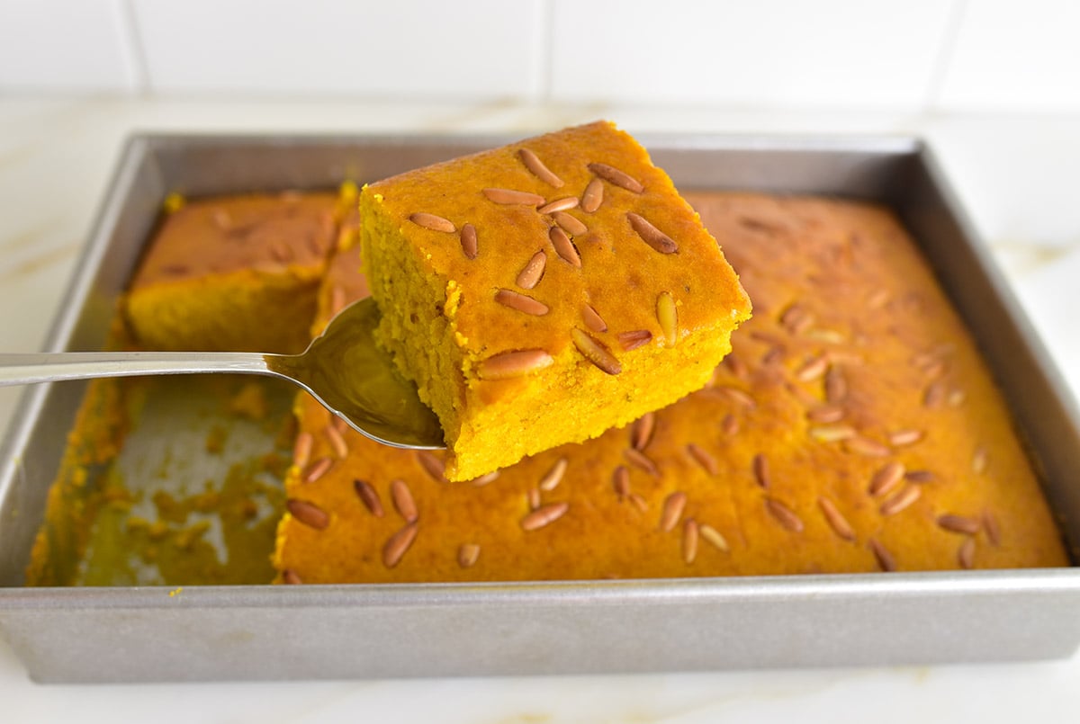 Bright orange cake slice on a cake server with the cake in the pan behind it