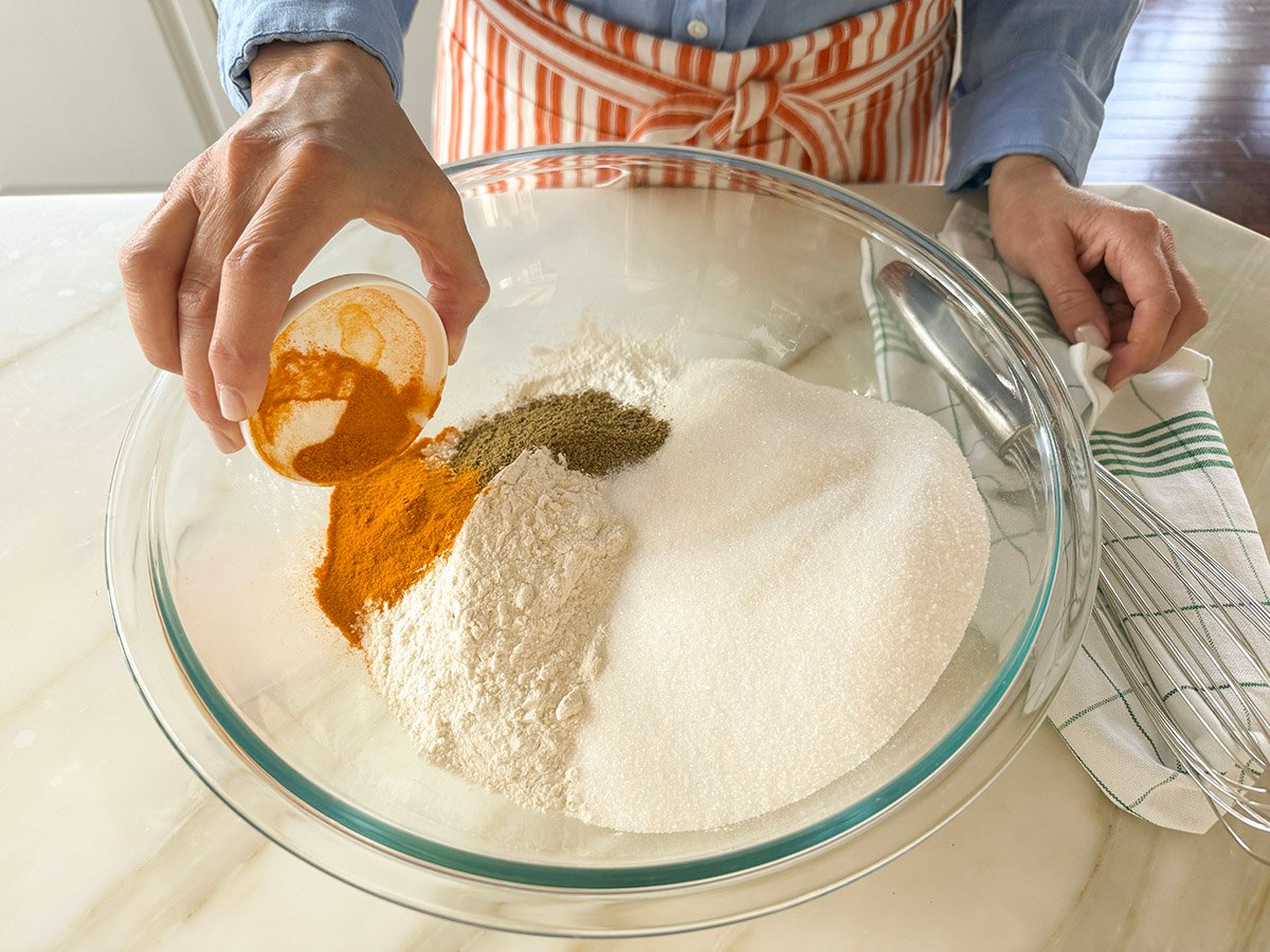 A hand pouring turmeric into a bowl of dry ingredients