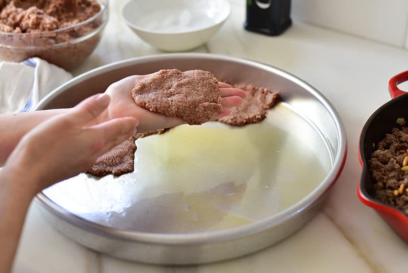 Lebanese kibbeh in a round pan, bottom layer smoothed with ice water