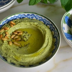 Green mint hummus swirled in a blue bowl with toasted pine nuts on top