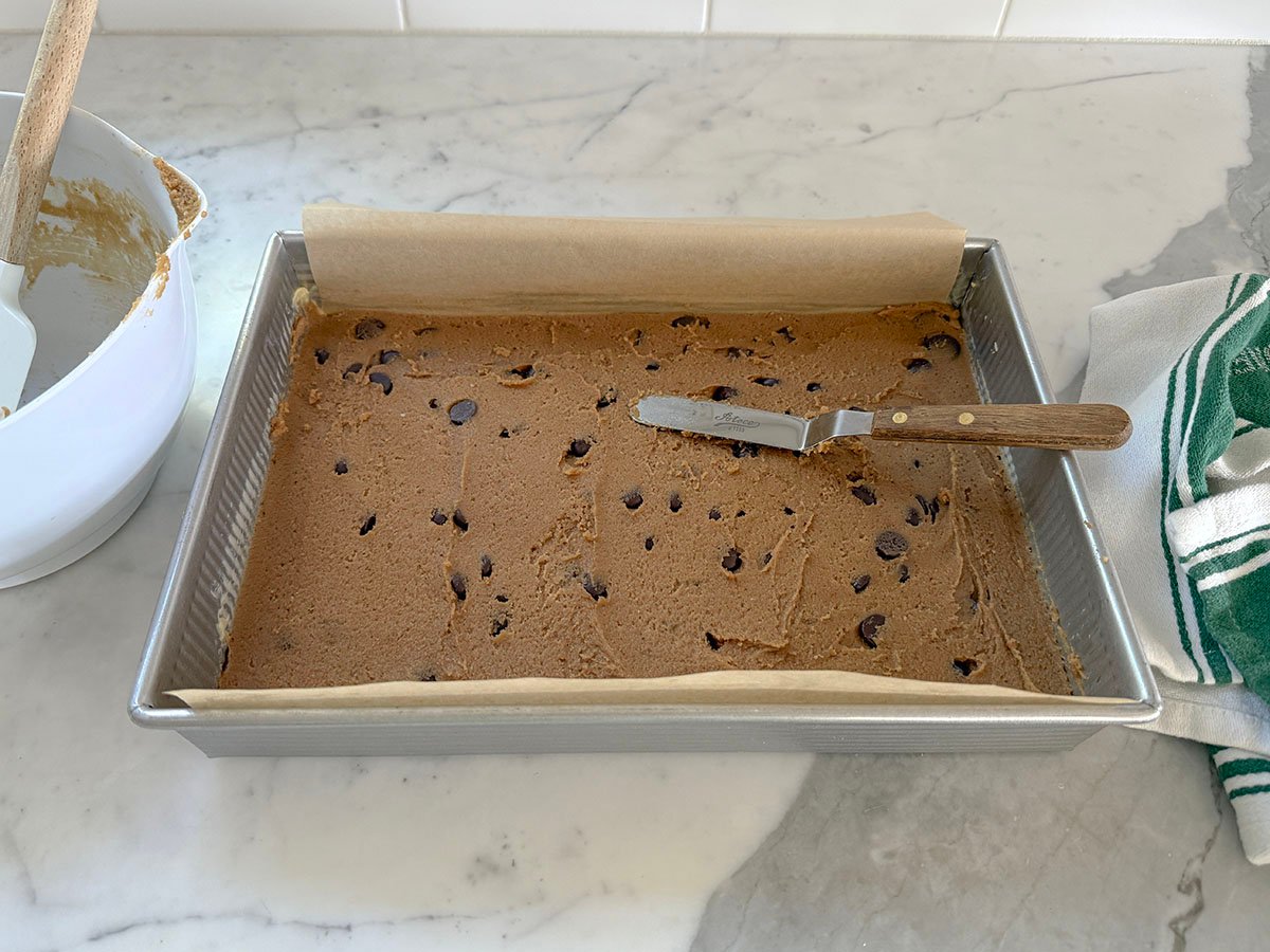 cookie dough spread in a parchment lined pan with an offset spatula