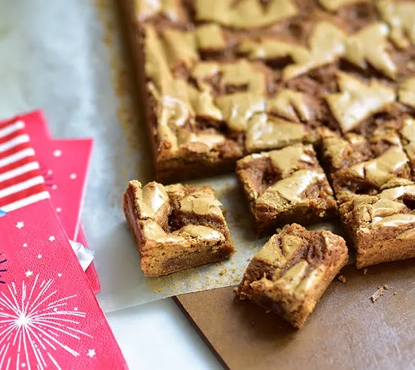Blondie bars with orange blossom caramel cut into pieces on a board with red white and blue napkins