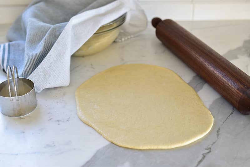 Fatayer dough rolled out with a dark wood rolling pin with bowl of dough on the side