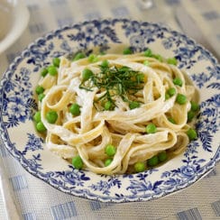 A blue and white bowl of pasta with green peas and herbs