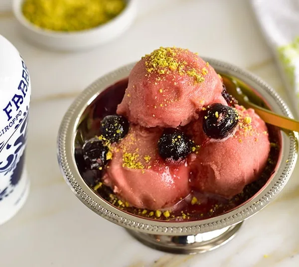 Scoops of cherry sorbet in a little silver cup with cherry sauce and pistachios on top