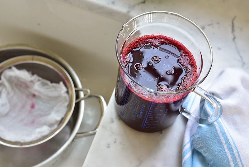 red raspberry juice in a tall measuring cup on the counter with a towel