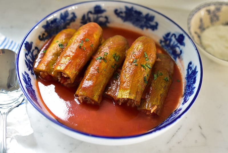 Green squash stuffed with rice with tomato broth in a blue and white bowl