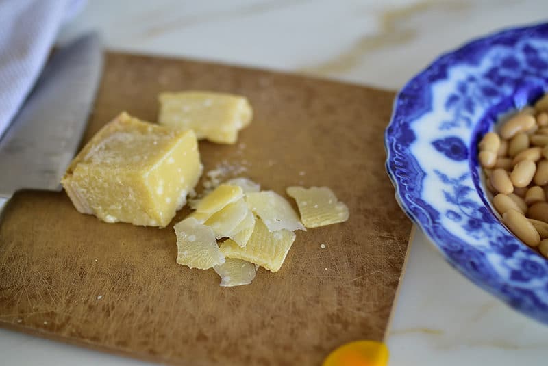 Thin slices of parmesan cheese on a cutting board, for a bowl of white beans