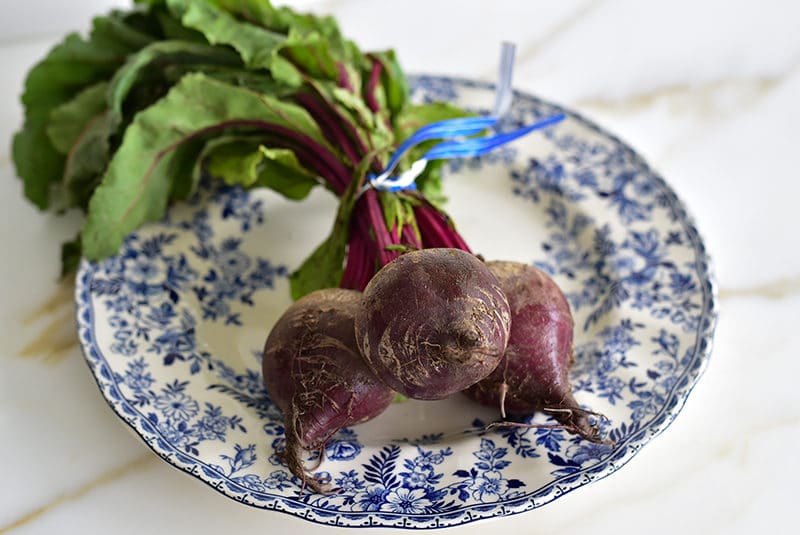 Red beets with greens on a blue and white plate