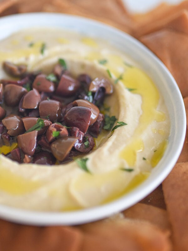 Hummus in a round bowl with olives in the middle of it