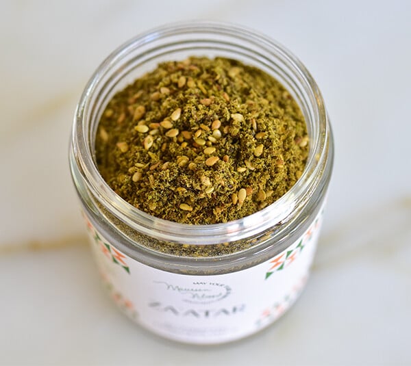 Open jar of za'atar spice on a marble counter