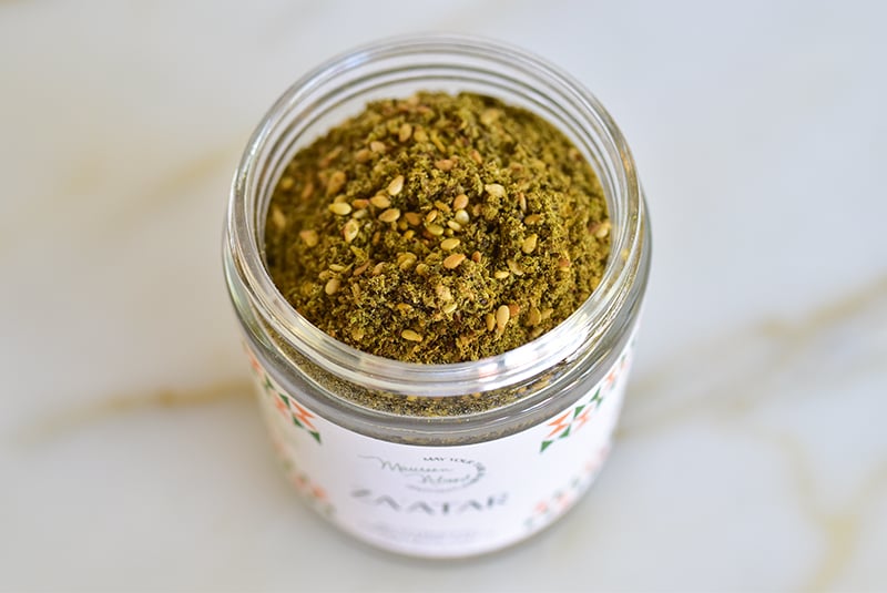 Open jar of za'atar spice on a marble counter
