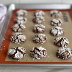 Chocolate crinkles with orange blossom on a sheet pan with a red and white towel on the side