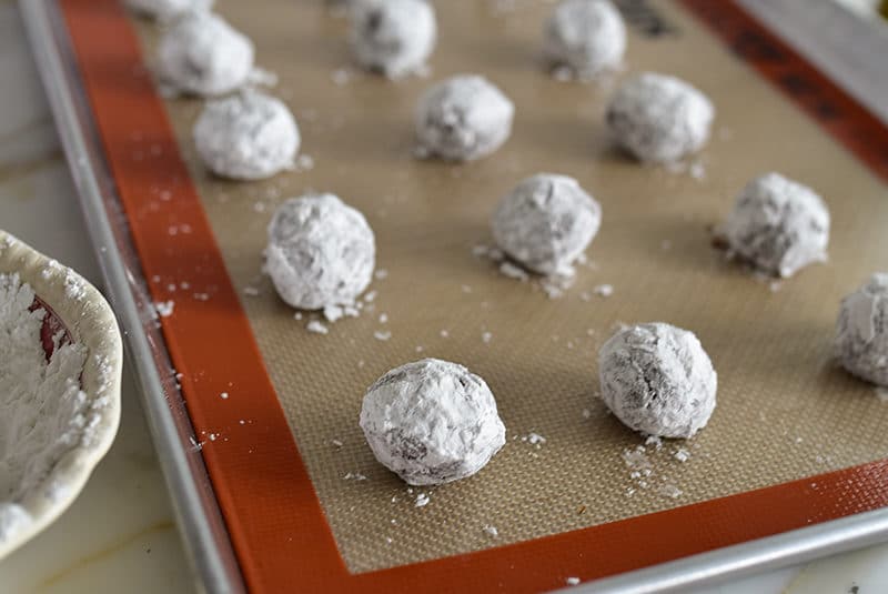 Chocolate crinkle balls in confectioners sugar on a sheet pan before baking