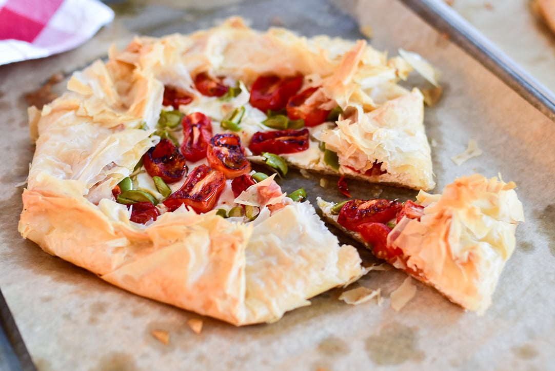 tomato galette on a baking sheet with one slice wedge