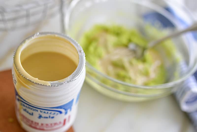 Tahini jar opened with avocado in a bowl