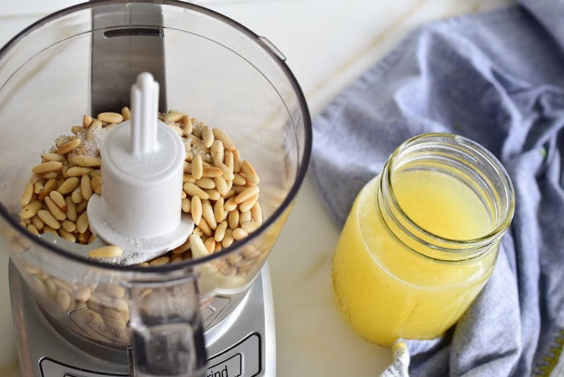 Pine nuts, garlic, and lemon in the food processor next to a jar of lemon juice