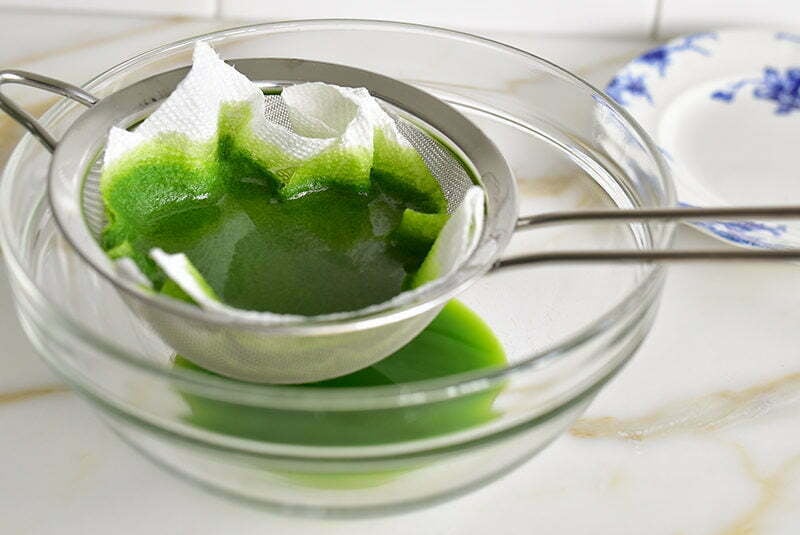 Basil oil in a strainer with a bowl underneath