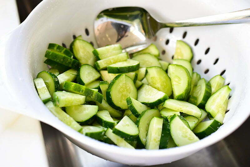 Sliced cucumbers draining in a white colander in the sink