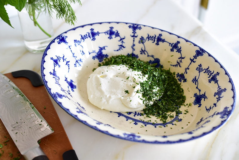 A blue and white bowl filled with labneh and herbs