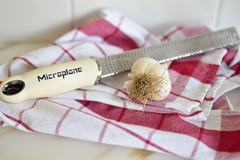 Head of garlic on a red plaid towel with a microplane grater
