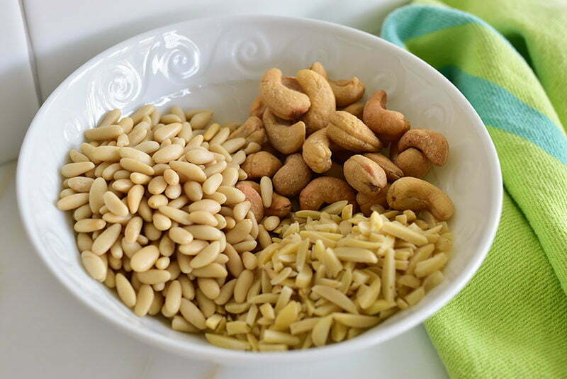 A white bowl with pine nuts, slivered almonds, and cashews