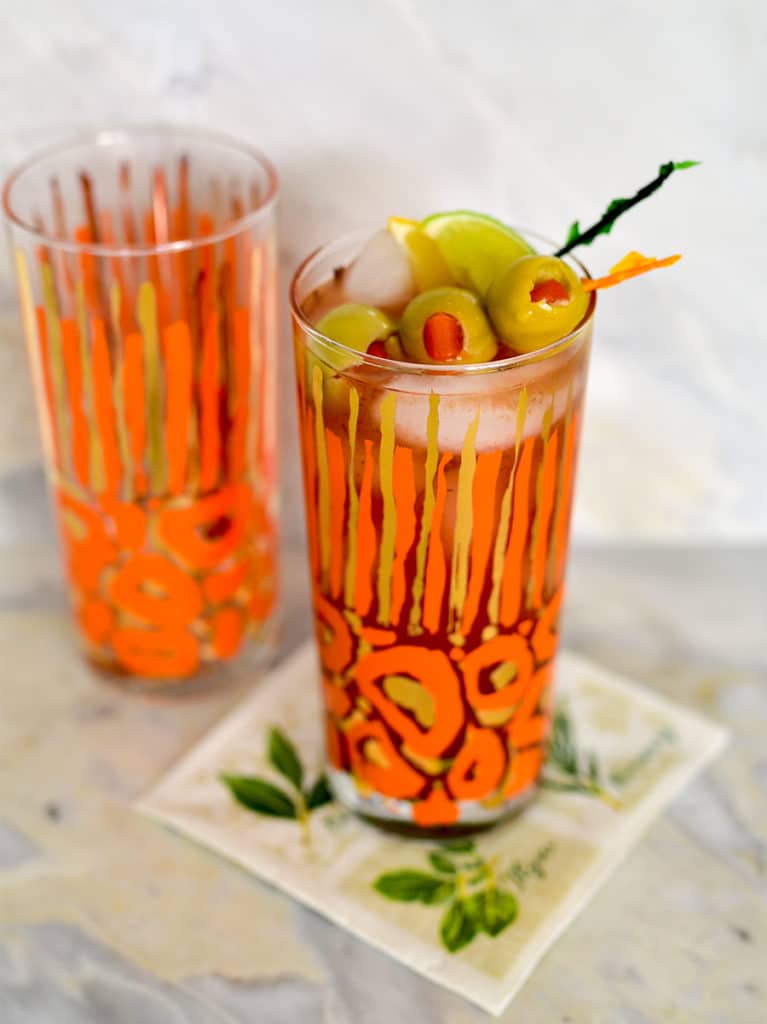 Bloody Mary Cocktail in an orange glass with garnishes on the bar