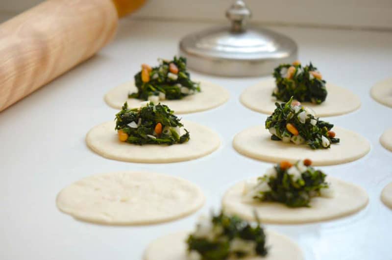 Spinach filling on cut dough rounds with rolling pin and cutter