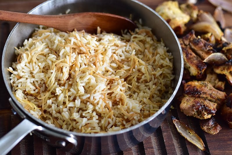 Lebanese rice in a pot with a wooden spoon and chicken shawarma