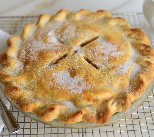 Apple pie on a rack with sugar and spoon