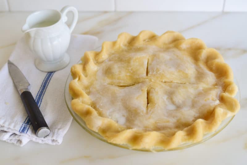 Crimped pie crust topped with milk before baking