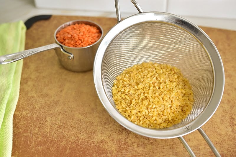 Bulgur and red lentils in a sieve on a cutting board