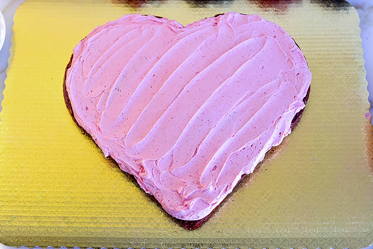 A heart cake on a gold board with pink frosting
