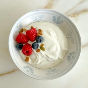 Homemade yogurt in a white bowl with raspberries and blueberries on top