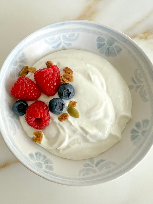 Homemade yogurt in a white bowl with raspberries and blueberries on top