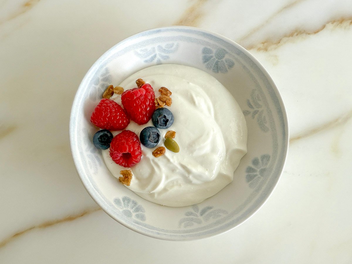 Homemade yogurt in a white bowl with raspberries and blueberries on top